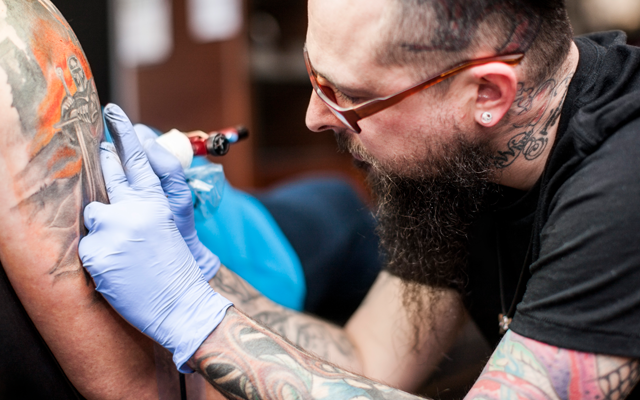 Man getting a tattoo on the arm from a bearded tattoo artist